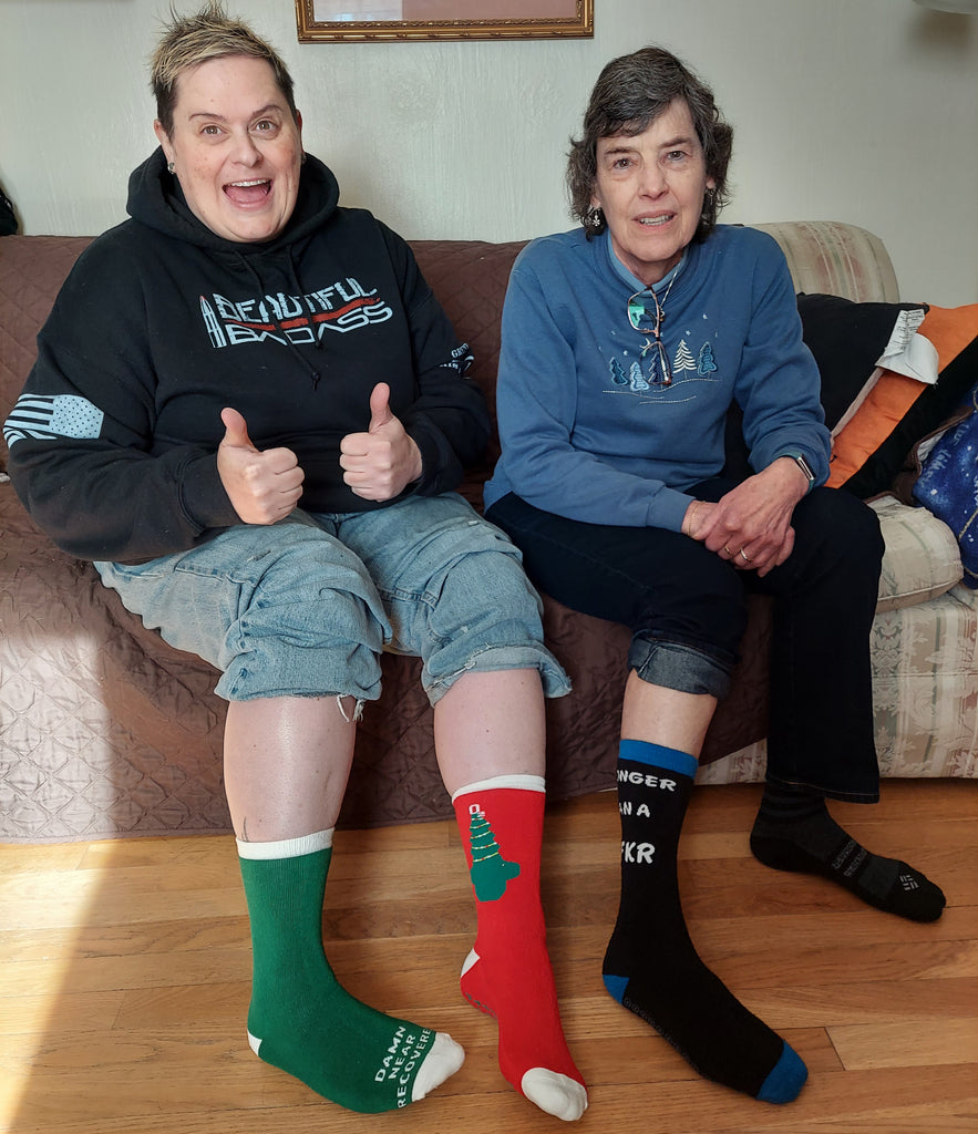 Two women lounging at home, wearing grip socks on a hardwood floor, smiling and enjoying slip-free comfort for fall prevention.